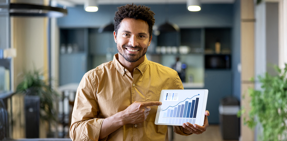 Smiling professional pointing to tablet displaying channel sales growth chart.