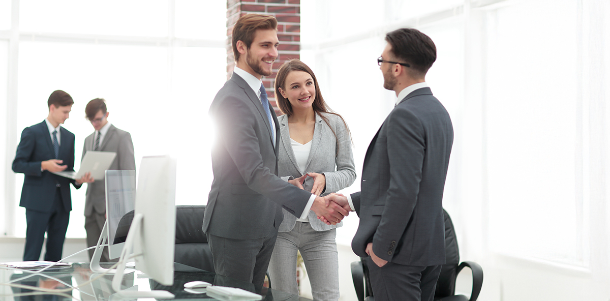 Business professionals in formal attire shaking hands and smiling in a modern office, symbolizing successful partnerships and consensus in channel sales.